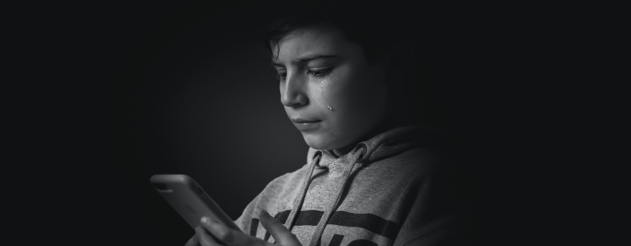Black and white photo of a child holding a cellphone and crying is a sign of experiencing Cyber Libel Philippines.